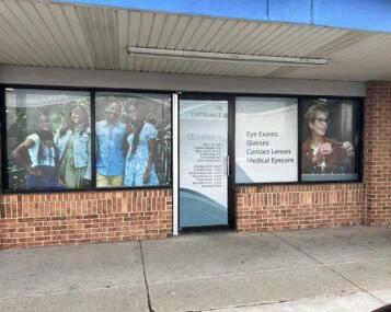 A storefront displays advertisements for eye care services, including pictures of smiling people and text listing eye exams, glasses, contact lenses, and medical eyewear.